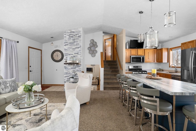 kitchen featuring appliances with stainless steel finishes, a center island, hanging light fixtures, vaulted ceiling, and light colored carpet