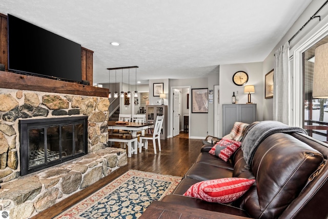 living room featuring a textured ceiling, a stone fireplace, and dark hardwood / wood-style flooring