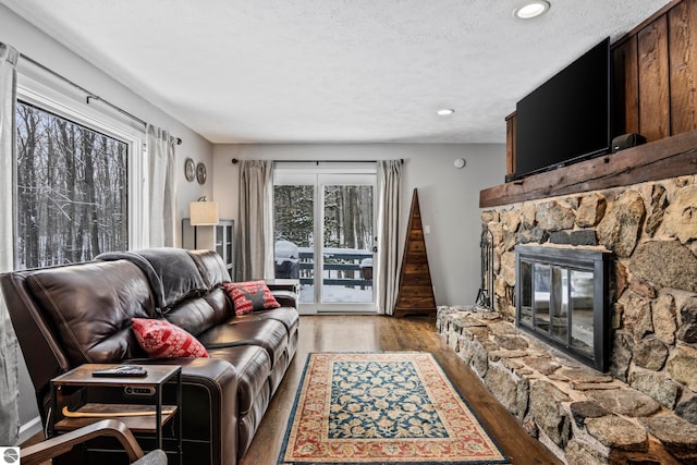 living room featuring wood-type flooring, a textured ceiling, and a stone fireplace