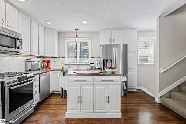 kitchen with appliances with stainless steel finishes, decorative light fixtures, white cabinetry, dark hardwood / wood-style flooring, and tasteful backsplash