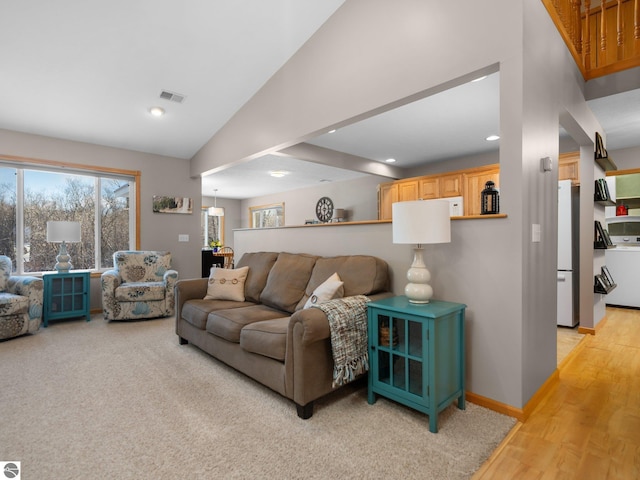 living room featuring light wood-type flooring, vaulted ceiling, and washer / clothes dryer