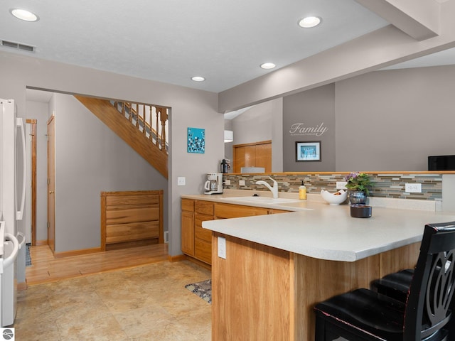 kitchen featuring kitchen peninsula, sink, backsplash, a breakfast bar, and white fridge