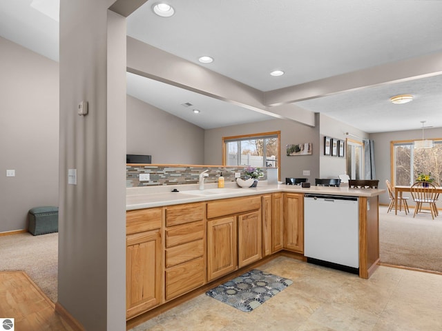 kitchen featuring white dishwasher, tasteful backsplash, sink, kitchen peninsula, and light colored carpet