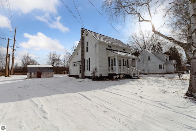 snow covered back of property with a porch and a shed