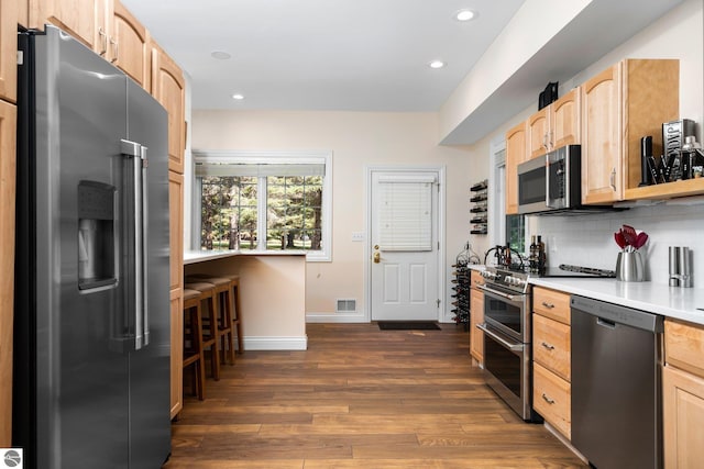 kitchen featuring light brown cabinetry, decorative backsplash, dark hardwood / wood-style floors, and stainless steel appliances