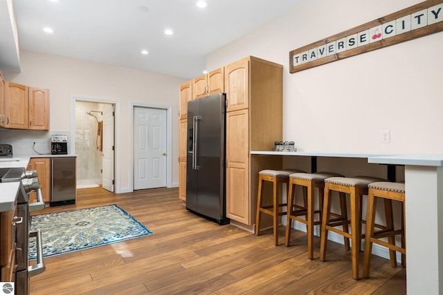 kitchen featuring appliances with stainless steel finishes, light brown cabinetry, decorative backsplash, light wood-type flooring, and a breakfast bar area