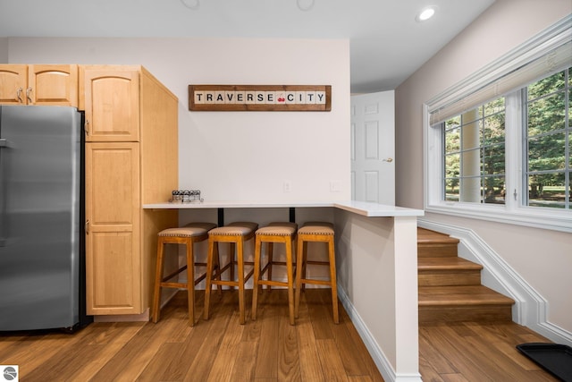 kitchen featuring light brown cabinets, light hardwood / wood-style flooring, a breakfast bar, and stainless steel fridge