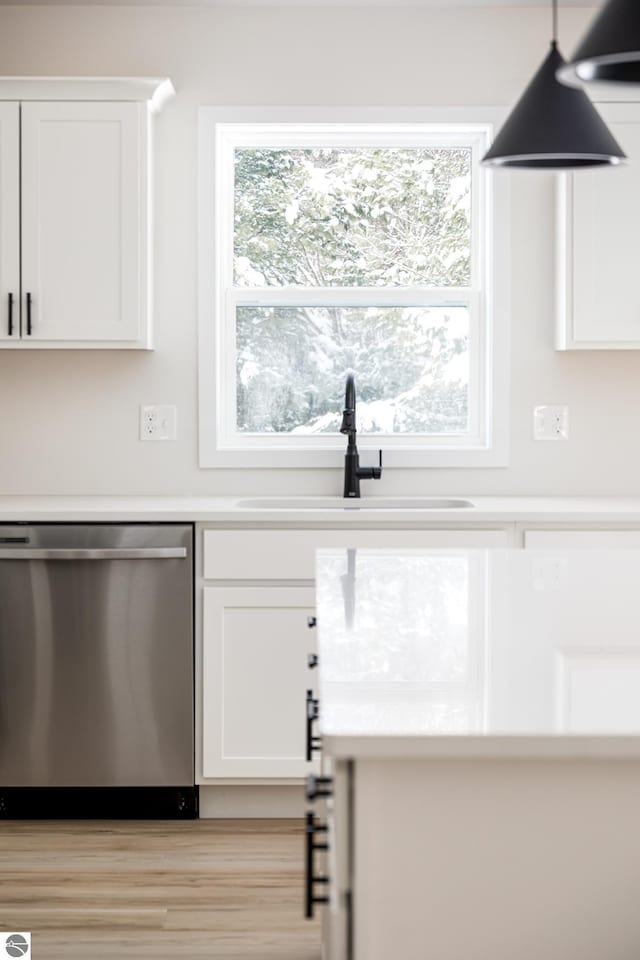 kitchen with sink, white cabinetry, hanging light fixtures, and stainless steel dishwasher