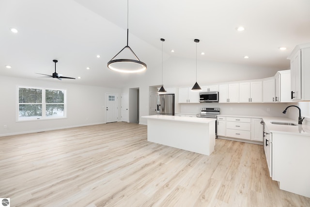 kitchen with white cabinets, appliances with stainless steel finishes, a kitchen island, decorative light fixtures, and sink