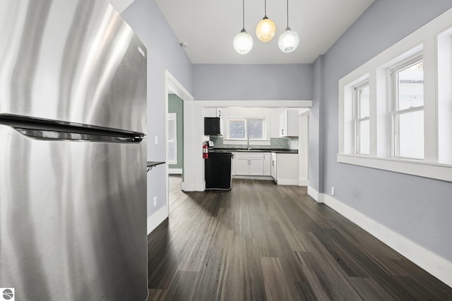 kitchen featuring pendant lighting, white cabinets, dark wood-type flooring, decorative backsplash, and stainless steel fridge