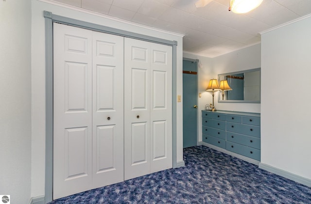 unfurnished bedroom featuring dark colored carpet, a closet, ceiling fan, and ornamental molding