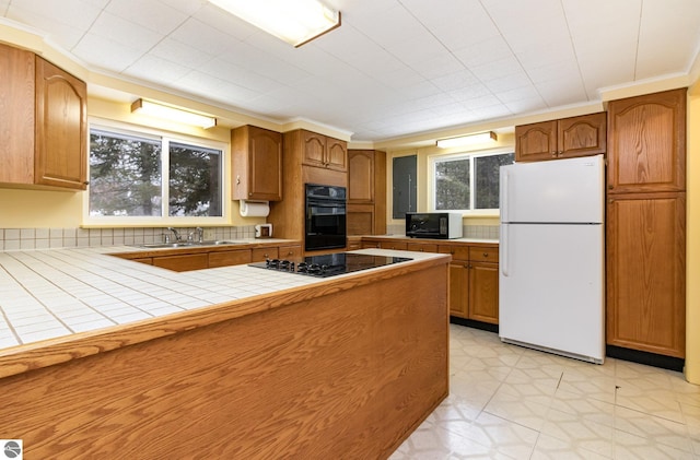 kitchen featuring black appliances, tasteful backsplash, sink, ornamental molding, and tile countertops