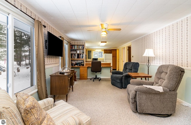 carpeted living room with crown molding, ceiling fan, and built in desk