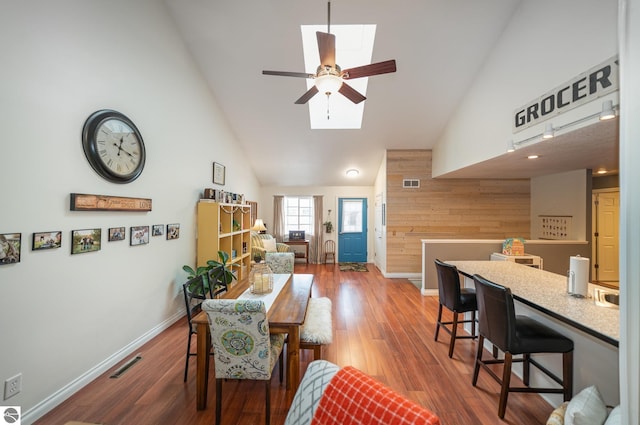 living room featuring dark wood-type flooring, wooden walls, high vaulted ceiling, and a skylight