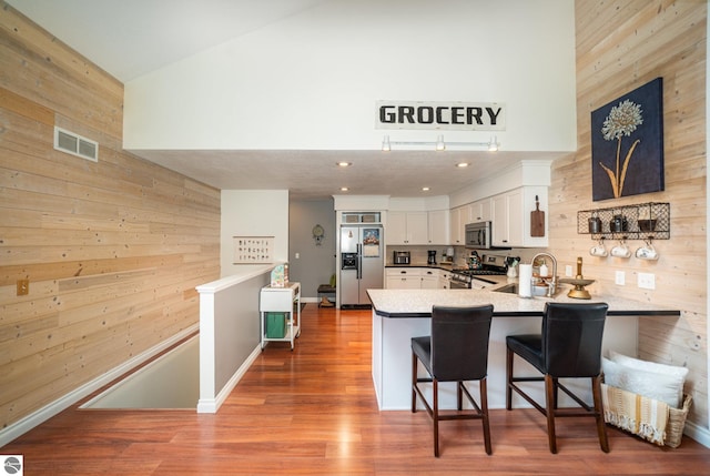 kitchen featuring appliances with stainless steel finishes, white cabinetry, kitchen peninsula, a breakfast bar, and wood walls