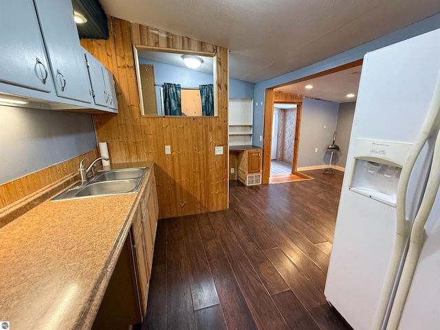 kitchen with sink, white fridge with ice dispenser, wooden walls, and dark hardwood / wood-style floors