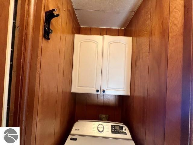 clothes washing area with cabinets, washer / clothes dryer, and wooden walls