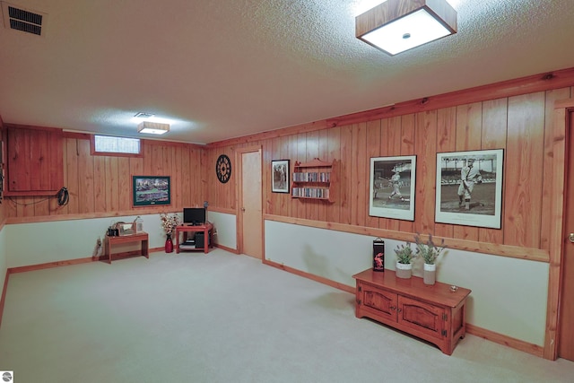 living area with a textured ceiling, light colored carpet, and wooden walls