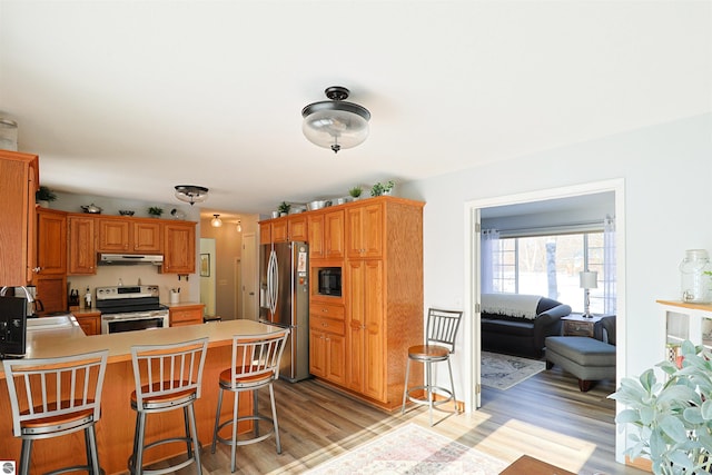 kitchen with kitchen peninsula, light wood-type flooring, a breakfast bar, and appliances with stainless steel finishes