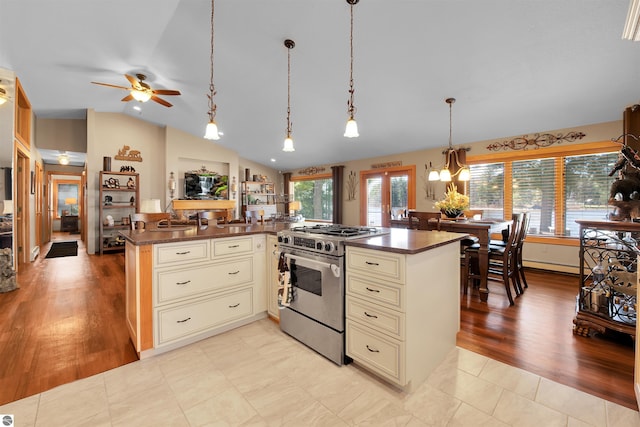 kitchen with pendant lighting, stainless steel range with gas cooktop, cream cabinets, a kitchen island, and lofted ceiling