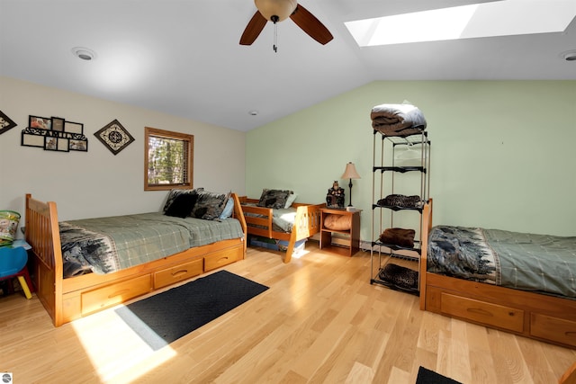 bedroom with ceiling fan, vaulted ceiling with skylight, and light hardwood / wood-style flooring