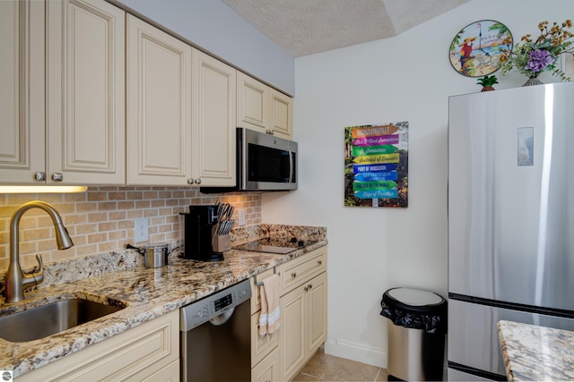 kitchen featuring sink, tasteful backsplash, light stone countertops, cream cabinets, and black appliances