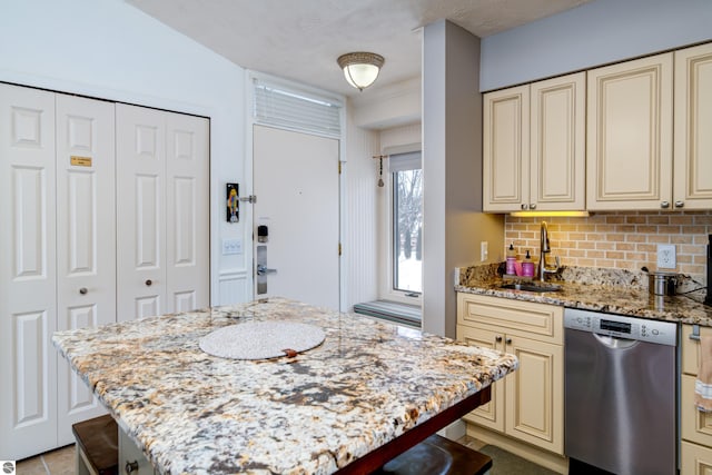 kitchen with cream cabinets, sink, a kitchen bar, stainless steel dishwasher, and light stone countertops