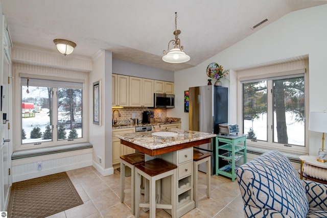 kitchen with a center island, vaulted ceiling, hanging light fixtures, appliances with stainless steel finishes, and light stone countertops