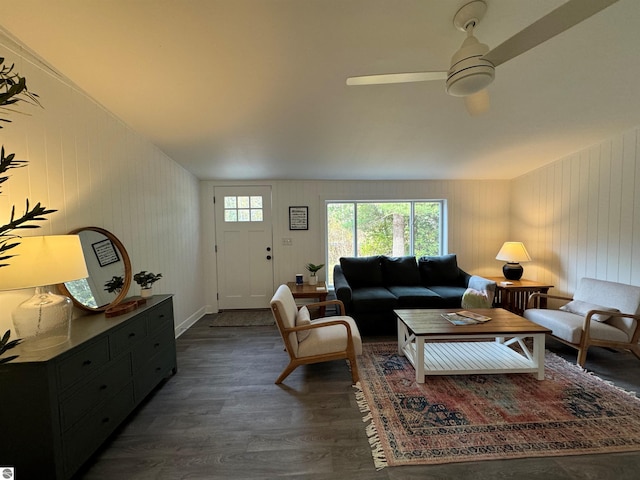 living room featuring dark wood-type flooring, ceiling fan, and wooden walls