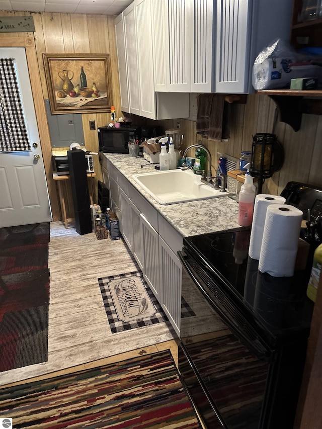 kitchen featuring sink, wood-type flooring, black appliances, wooden walls, and white cabinets