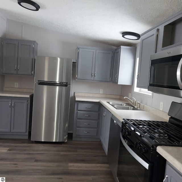 kitchen with appliances with stainless steel finishes, sink, gray cabinetry, dark wood-type flooring, and a textured ceiling