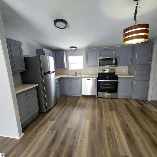 kitchen with sink, appliances with stainless steel finishes, gray cabinetry, hanging light fixtures, and dark hardwood / wood-style flooring