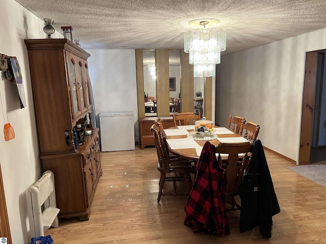 dining room with an inviting chandelier, radiator heating unit, a textured ceiling, and light wood-type flooring