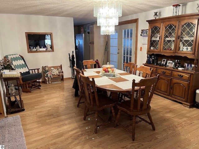 dining room with light hardwood / wood-style floors, a chandelier, a textured ceiling, and french doors