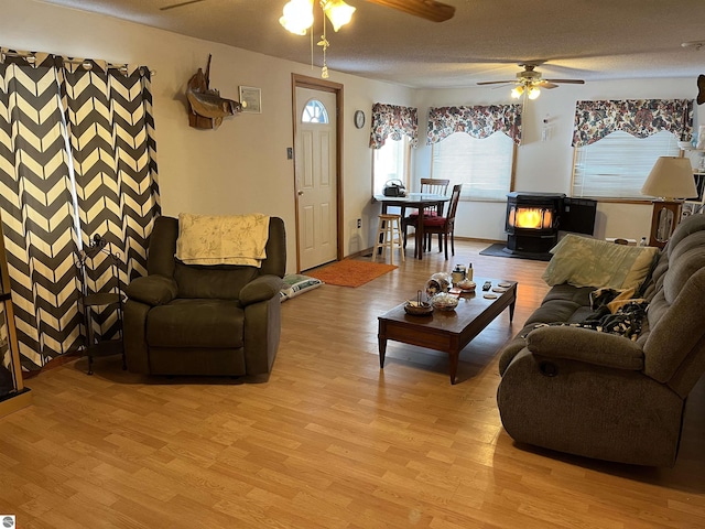 living room with ceiling fan, a wood stove, a textured ceiling, and light hardwood / wood-style flooring