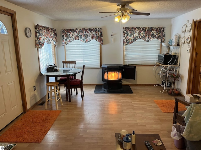 dining space with ceiling fan, a wood stove, a textured ceiling, and light hardwood / wood-style flooring