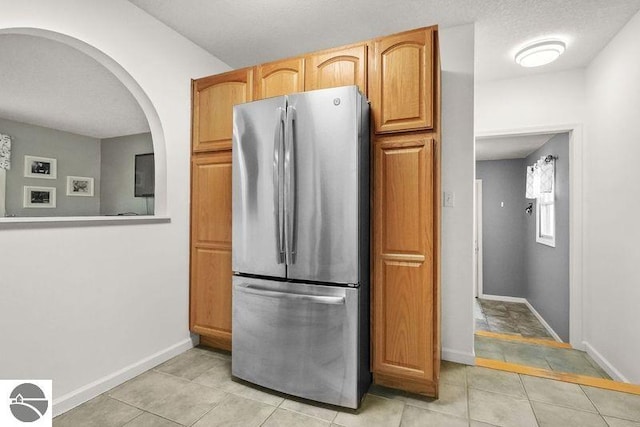 kitchen with stainless steel fridge, light brown cabinetry, a textured ceiling, and light tile patterned floors