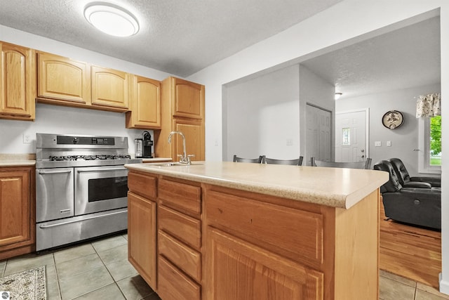 kitchen featuring sink, gas stove, a textured ceiling, a center island with sink, and light tile patterned flooring