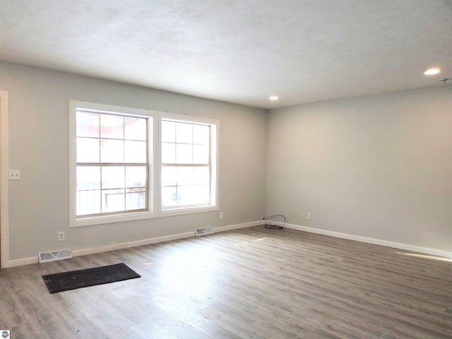 spare room with hardwood / wood-style floors, a wealth of natural light, and a textured ceiling