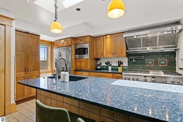 kitchen with hanging light fixtures, dark stone countertops, a kitchen breakfast bar, stainless steel appliances, and exhaust hood