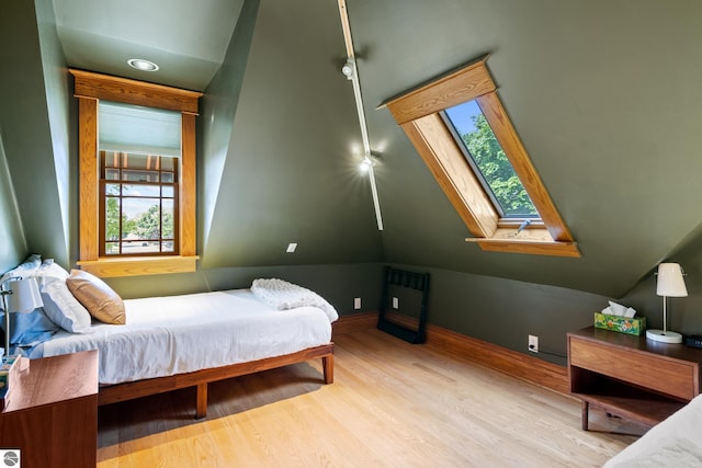 bedroom featuring vaulted ceiling with skylight and light hardwood / wood-style floors