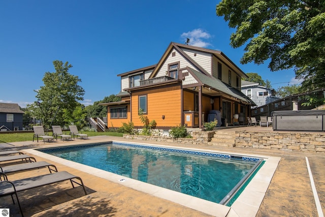 rear view of property featuring a swimming pool with hot tub, a patio, and a balcony