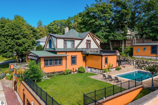 rear view of property featuring a fenced in pool, a balcony, and a lawn