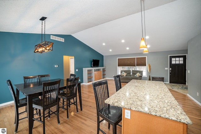 kitchen featuring light stone countertops, pendant lighting, lofted ceiling, and light hardwood / wood-style floors