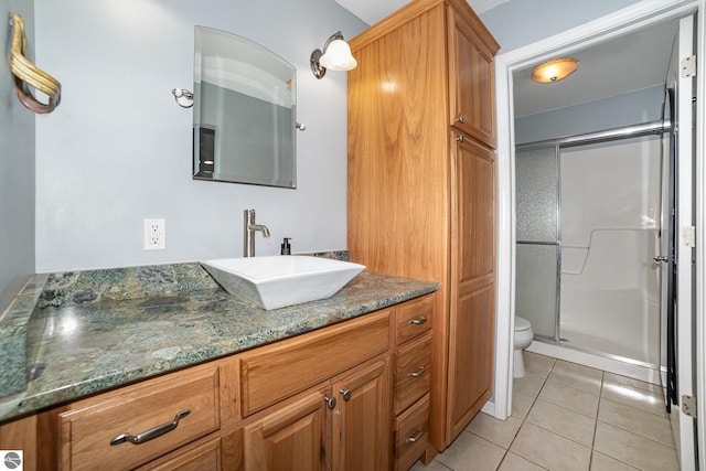 bathroom with a shower with door, vanity, tile patterned flooring, and toilet