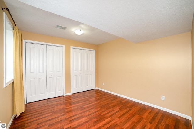 unfurnished bedroom featuring multiple closets, dark hardwood / wood-style floors, and a textured ceiling