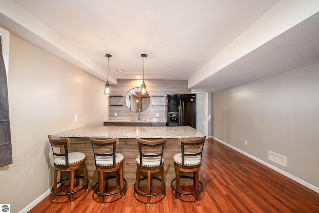 bar with pendant lighting, sink, dark hardwood / wood-style flooring, light stone counters, and black fridge