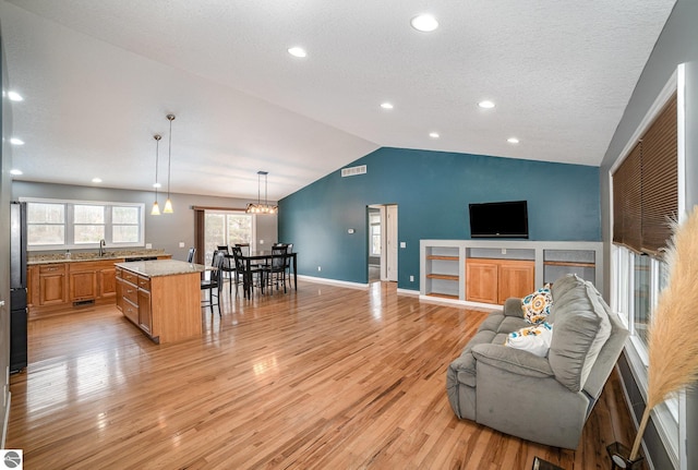 living room featuring sink, vaulted ceiling, a textured ceiling, light wood-type flooring, and a notable chandelier