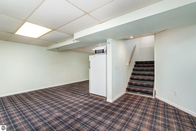 basement featuring white refrigerator and a drop ceiling