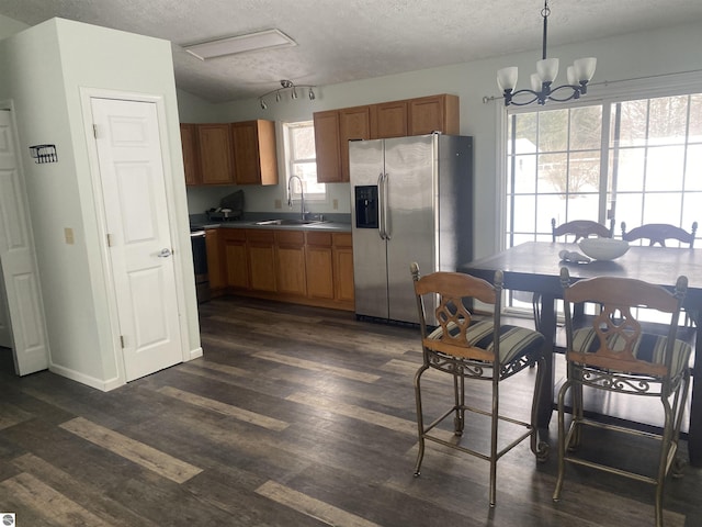 kitchen featuring dark wood-type flooring, sink, decorative light fixtures, stainless steel fridge, and a notable chandelier